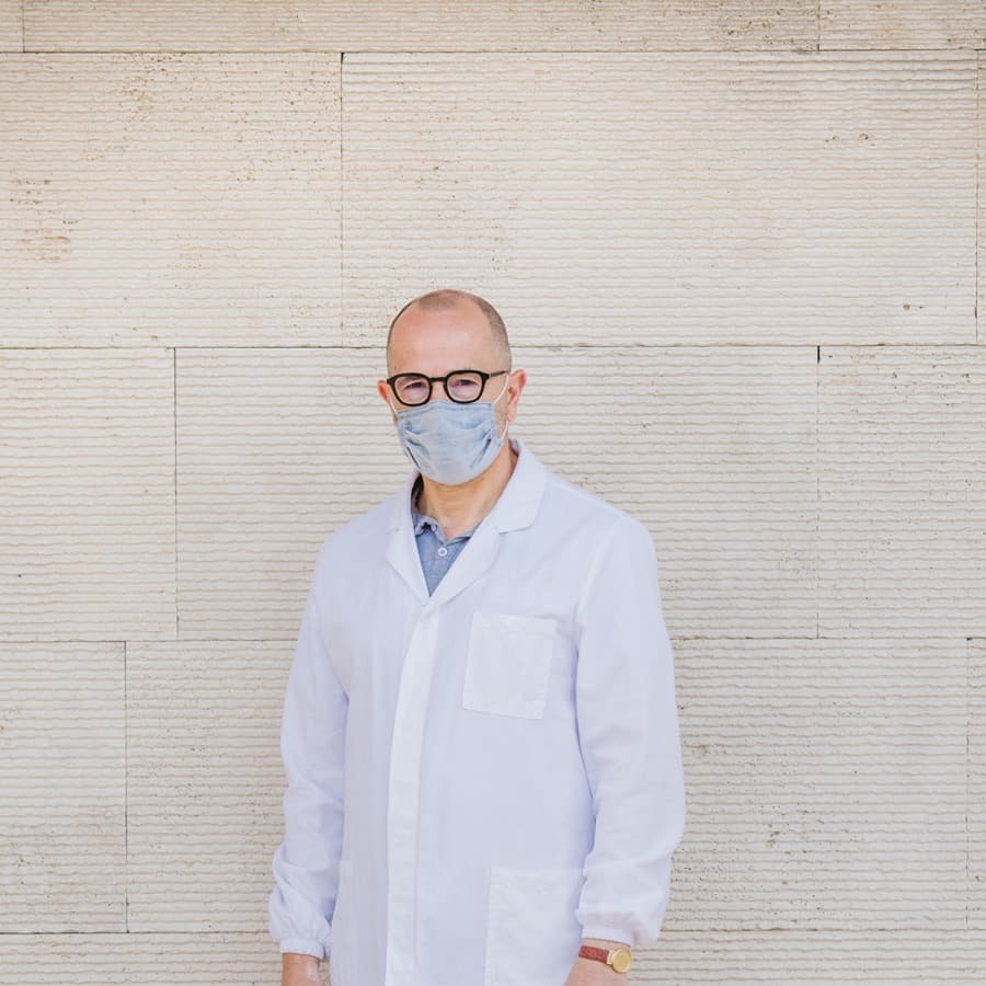 Un uomo in camice bianco indossa la mascherina chirurgica azzurra AV Mask davanti a un muro di pietra chiara.